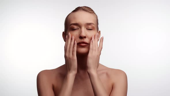 Beautiful Woman Stands in Studio on White Background and Rubs Makeup on Cheeks Front View