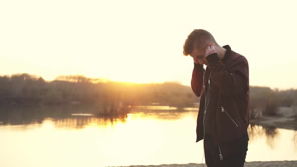 Young Handsome Man Wearing Headphones Listens to Music Walks on Beach During Sunset