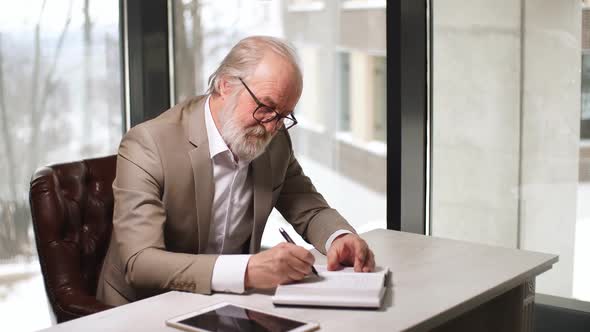 Old Man Pleasant Man Is Writing His Ideas in the Notebook Indoors.