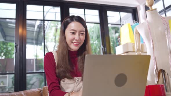 Asian female shop owner checking customer order and happy to receiving good news on laptop