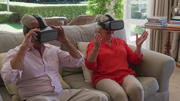 Caucasian senior couple sitting on couch in living room using vr headsets