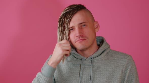 Young Handsome Man with Blonde Dreadlocks Preening Himself in Front of Camera on Pink Background