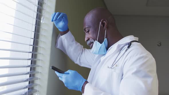 Portrait of african american male doctor wearing face mask talking using smartphone