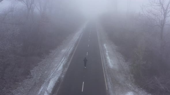 Sporty Man in Tracksuit Runs Along Road Surrounded By Frost Trees in Winter in Foggy Weather