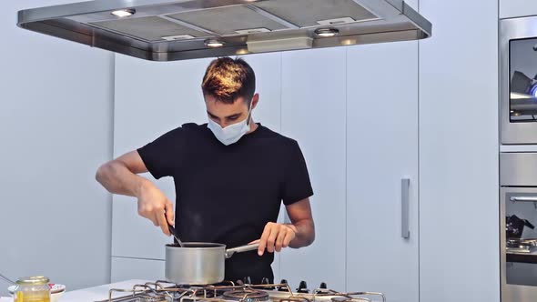 Young man at home preparing food with protective mask. Healthy food in quarantine. Stay at home and