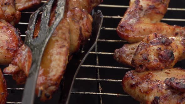 Closeup of Chicken Wings on Skewers Rotated with Kitchen Tongs on the Grill