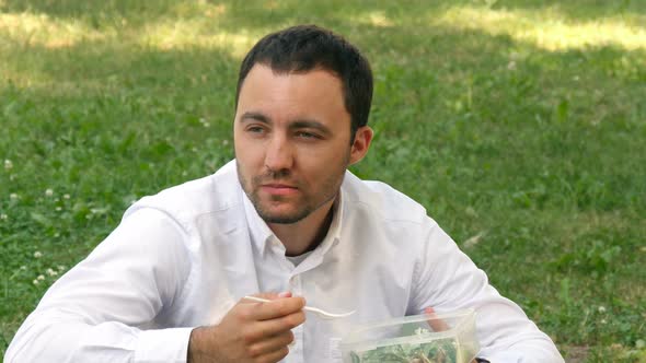 Man Drinking Water Sitting in a Beautiful Green Field on a Sunny Day