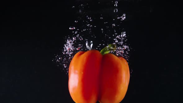 Red Bell Pepper Falls Down in Clear Water with Bubbles