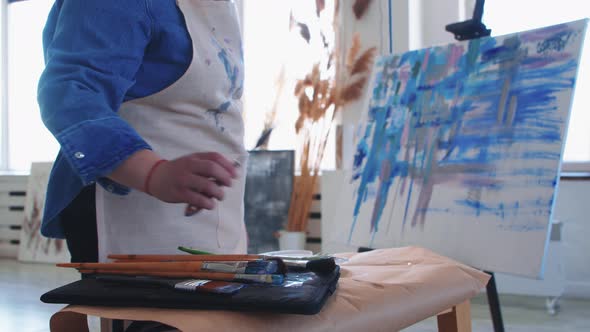 A Woman Paint Artist Taking a Brush and Drawing a Colorful Mostly Blue Painting on a Canvas