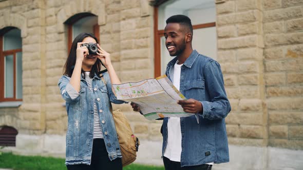 Happy African American Guy and Caucasian Girl Travelers Are Looking at Map and Taking Photos