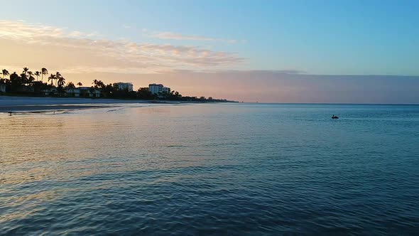 Flying above the waves at the beach looking at the beautiful sunrise with pelicans swimming in the d