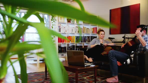 Man playing guitar while woman reading book