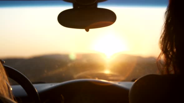 Two Young Women Watch the Sunset Sitting in the Car Setting Sun Rays Paint Optical Flares