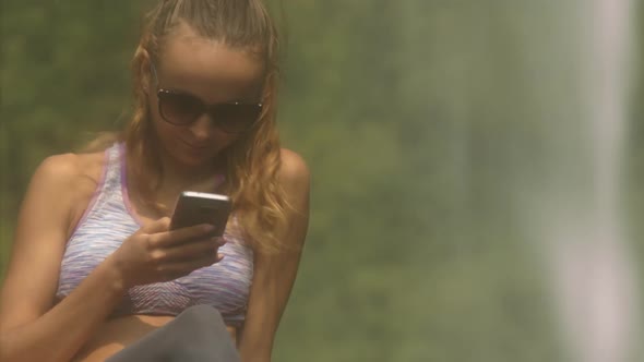 Blonde Lady in Sunglasses Texts Sms By Waterfall Closeup