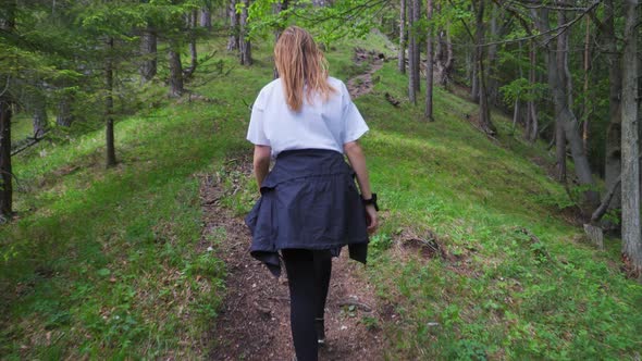 Female Hiker Climbing On An Uphill Trail With Trees In The Mountain. - rear follow