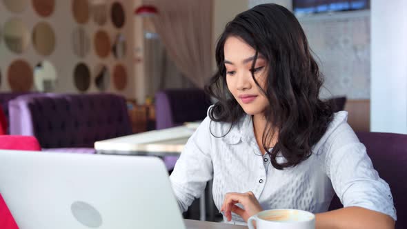 Asian Businesswoman Thinking and Looking at Screen and Typing Text Using Laptop