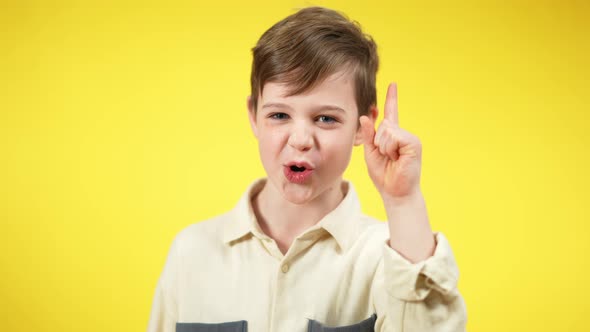 Little Brunette Boy Shaking Finger Looking at Camera Standing at Yellow Background