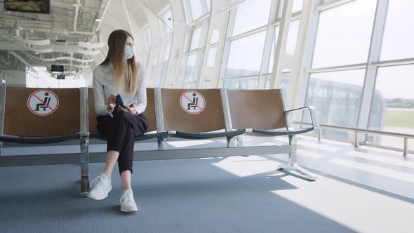 Confident Business Woman in a Mask Sitting at the Airport Holding a Passport and