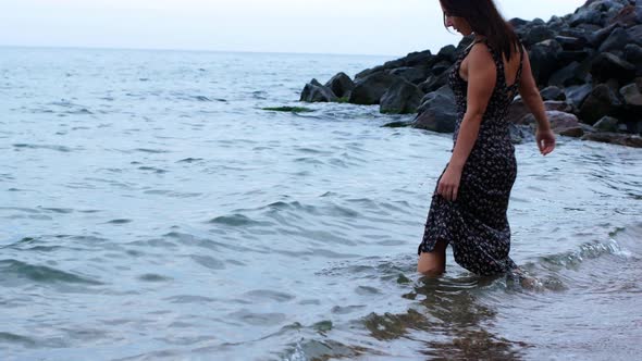 A woman in a long dress bathes in the sea. A beautiful girl in a beautiful outfit walks along