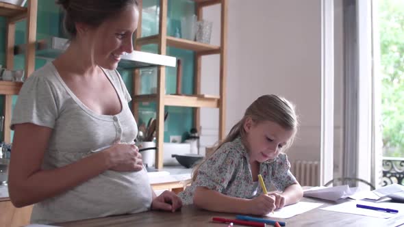 Expectant mother watching as her young daughter practices writing