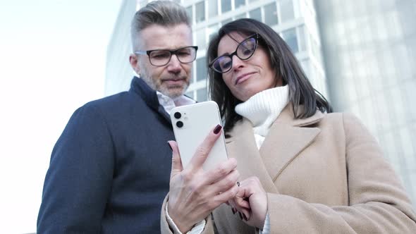 Business man and woman browsing phone in modern city district