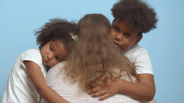 Back View of Woman Hugging Her Preschool Son and Daughter Isolated Over Blue Background