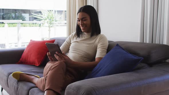 Mixed race gender fluid person sitting on couch and using tablet at home