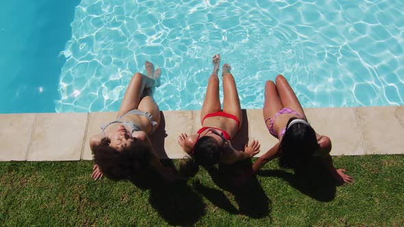 Diverse group of female friends sitting at the poolside sunbathing