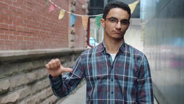 Slow Motion Portrait of Unhappy Middle Eastern Man Showing Thumbsdown Hand Gesture Outdoors