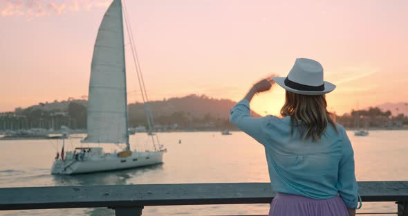 Back View of Cheerful Woman Waving To People on Sailing Ship at Sunset,  Trip