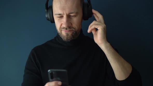 A Young Man Listens to Music on Headphones Through an Application in a Smartphone