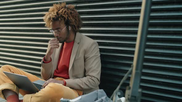 Afro Man Sitting on Street and Working on Laptop