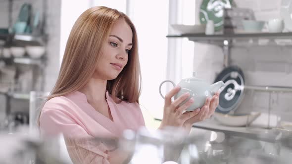 The Young Woman Is Looking at the Glass Teapot at the Tableware Store