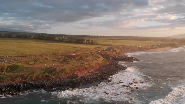 A drone flies over the ocean waves  and into Maui Hawaii's Ho'okipa beach overlook at sunset near Pa