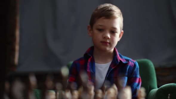 Portrait of Smart Little Boy Playing Chess Sitting at Home in Dark Living Room