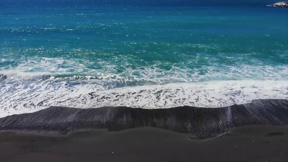 Waves hitting the beach with foam in slow motion, seen from above, tilting down while the POV is ris