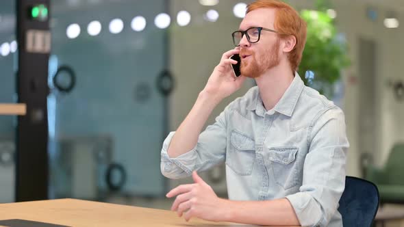 Cheerful Young Redhead Man Talking on Smartphone in Office