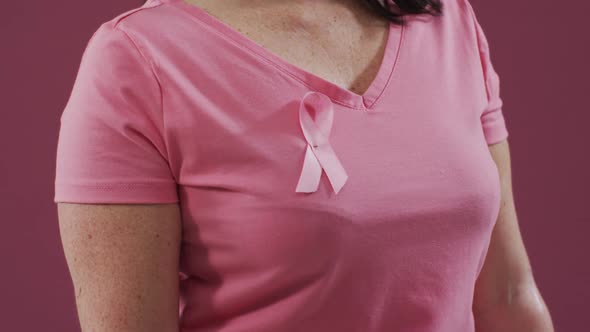 Mid section of a woman with pink ribbon on her chest clenching her fist against pink background