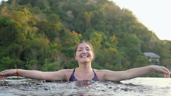 Smiling Brunette Makes Water Drops in Hotel Swimming Pool