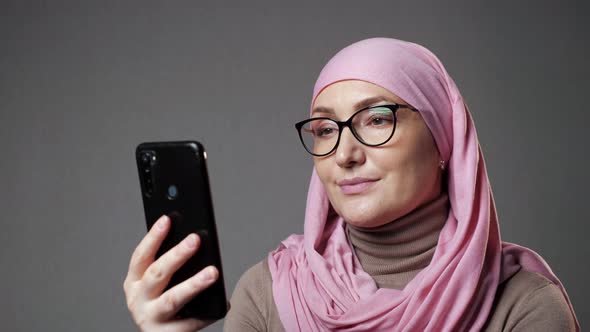 Young Muslim Woman in Hijab Smiles Watching Show Using Phone