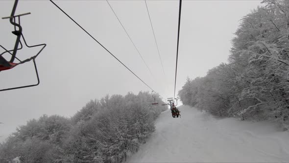 Ascending on a Chair Lift with Trees Covered in Snow on a Cloudy Day with Chairlifts Passing By