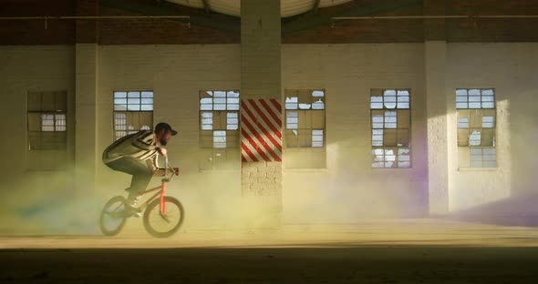 BMX riders in an empty warehouse using smoke grenade