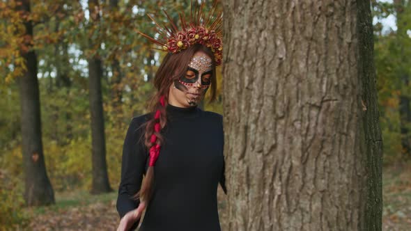 A Young Woman with Santa Muerte Makeup Dressed in a Black Dress of Death Walks Against the Backdrop