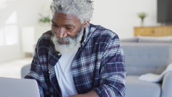 African American senior man sitting by a table, using laptop and smiling, social distancing and self