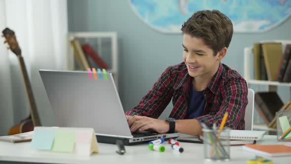 Teen Boy Actively Chatting With Friends in Social Networks Sitting in His Room