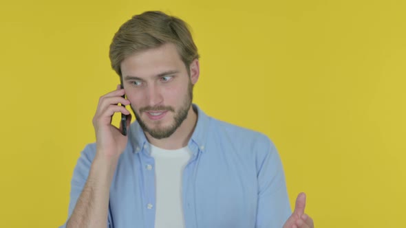 Young Man Talking Angry on Phone on Yellow Background