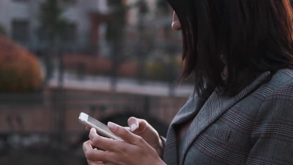 Portrait of a Confident Business Woman in a Suit Uses a Smartphone Outdoors