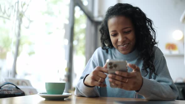 Smiling African woman wearing blue sweater leafing tape on phone