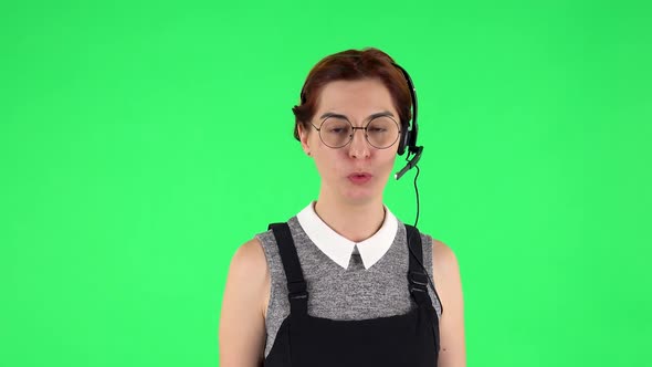 Portrait of Funny Girl in Round Glasses Is Talking on Headphones, Call Center. Green Screen