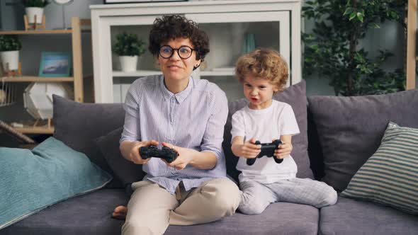 Mother and Young Child Playing Video Game on Couch at Home Laughing Having Fun